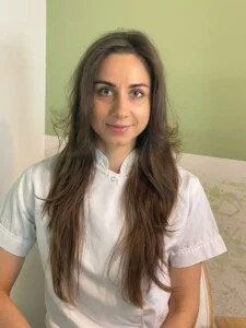 Smiling woman in white shirt in front of green wall.